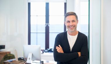 A smiling person standing in front of a desk.