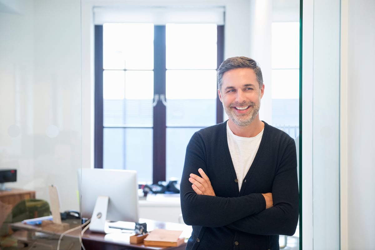 A smiling person standing in front of a desk.
