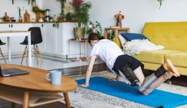 person facing away from the camera with a prothetic leg performing a push up from their knees on a blue exercise mat in a living room setting with a yellow sofa behind them.