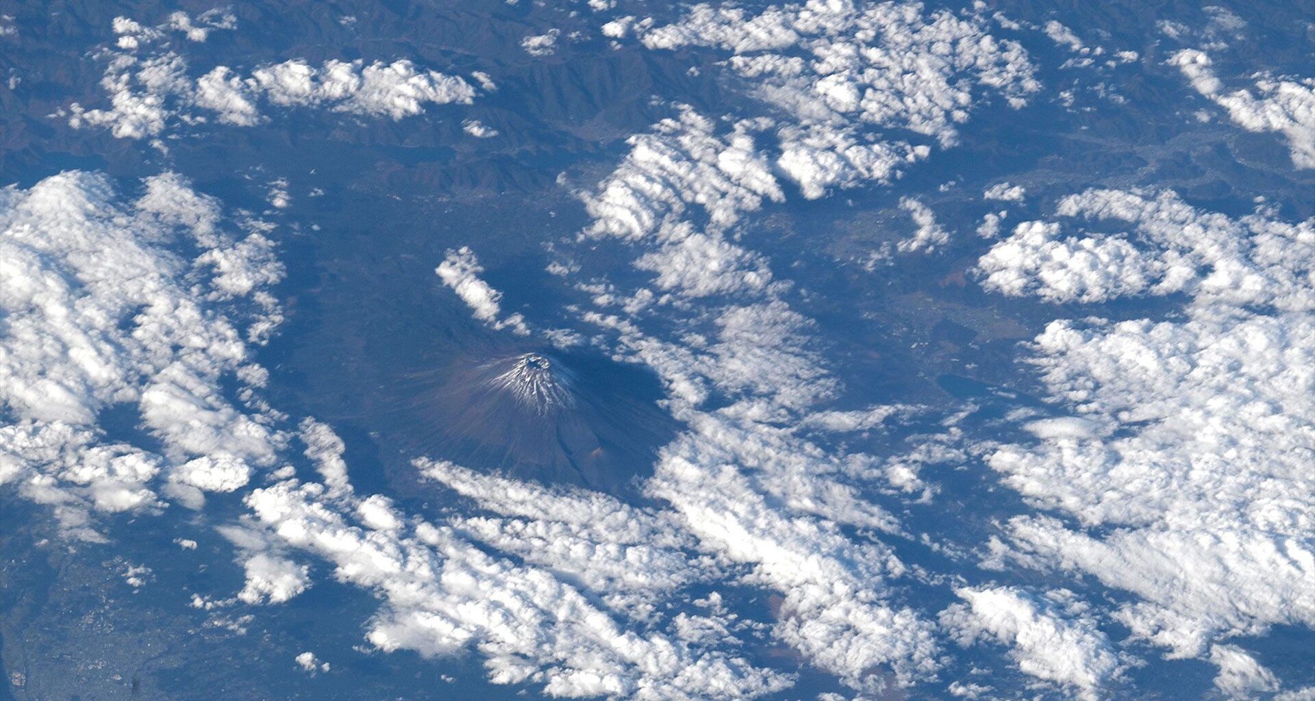 the snow-capped peak of a mountain is seen from far above the clouds in a photo taken by an astronaut on a space station.