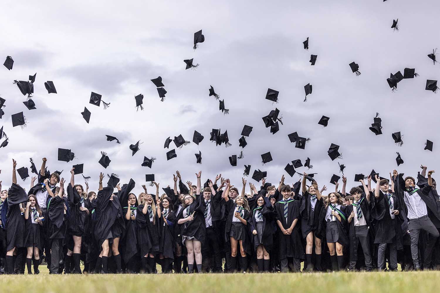 Students in graduation gowns celebrate by throwing mortarboards into the air.