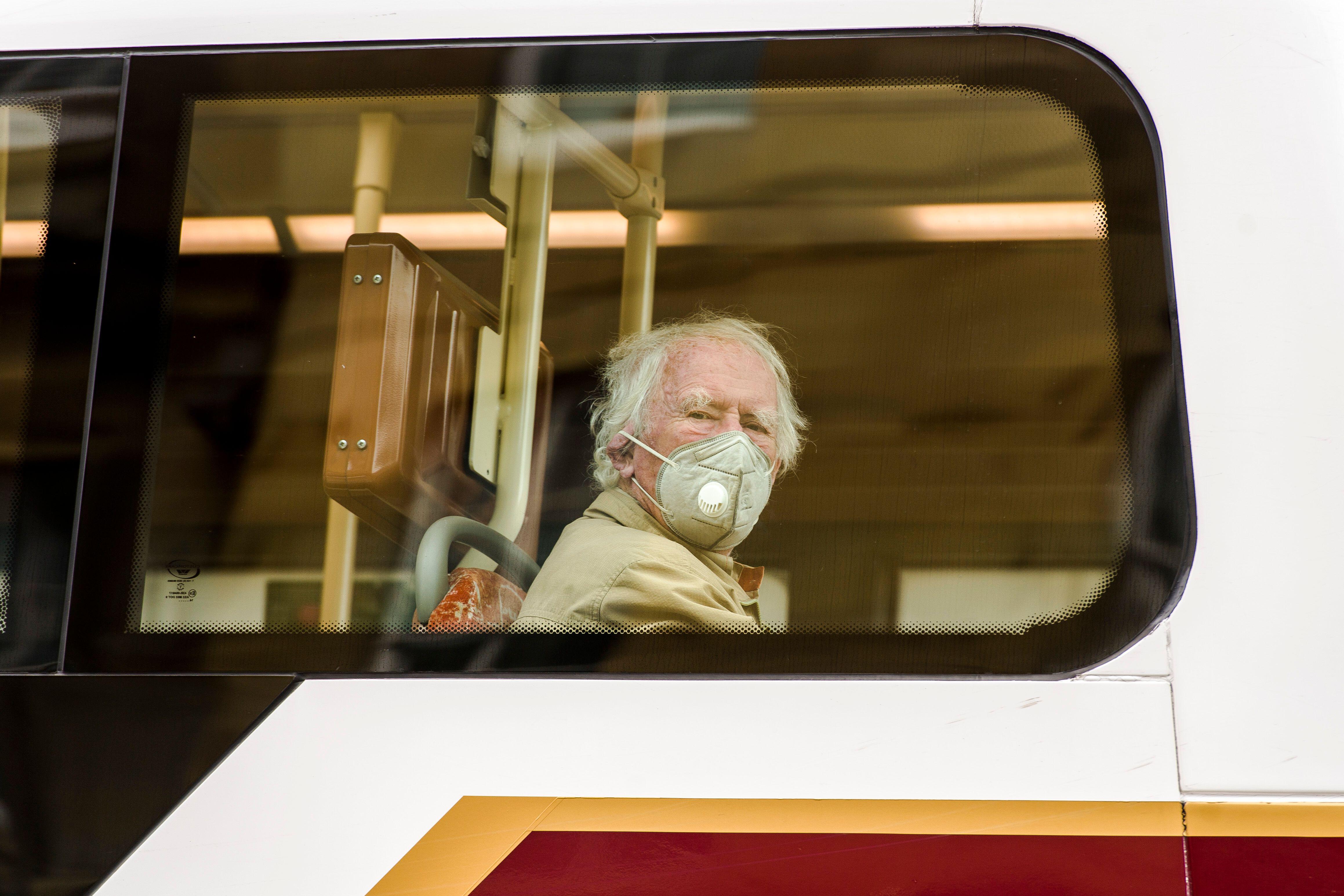 A man wearing a face mask looks out the window of a bus.