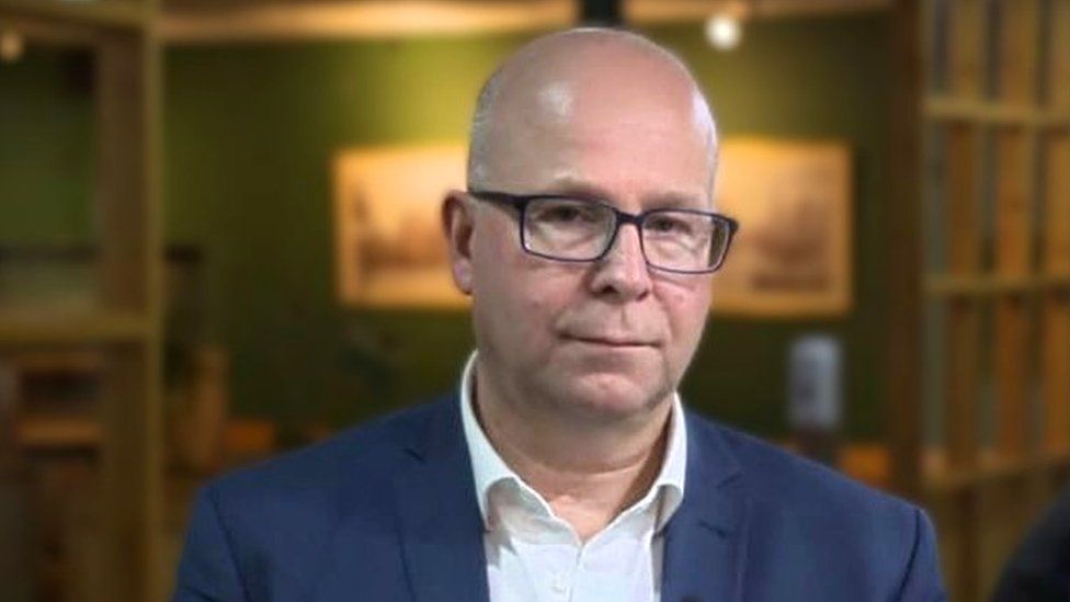 Andrew Buist, a bald man wearing glasses, a blue suit jacket, and a white shirt.