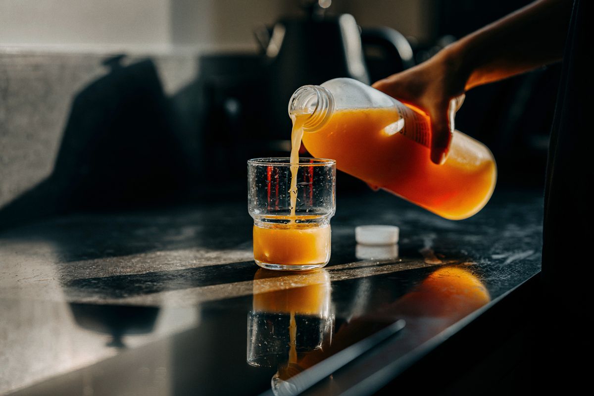 Cropped shot of a female hand pours a plastic bottle of fresh orange juice