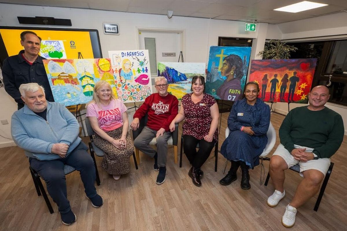 A group of people of mixed ages sitting in front of paintings on easels 