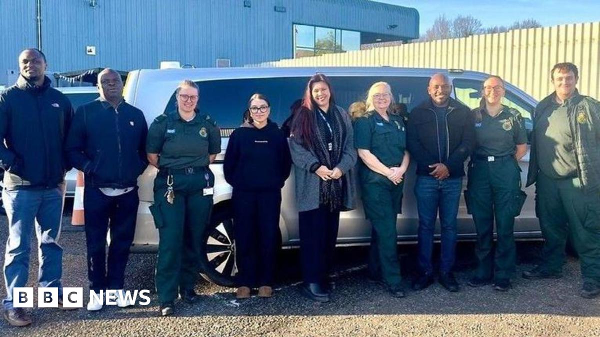 A group of nine staff, including paramedics stood together outside a large silver car with darkened windows.