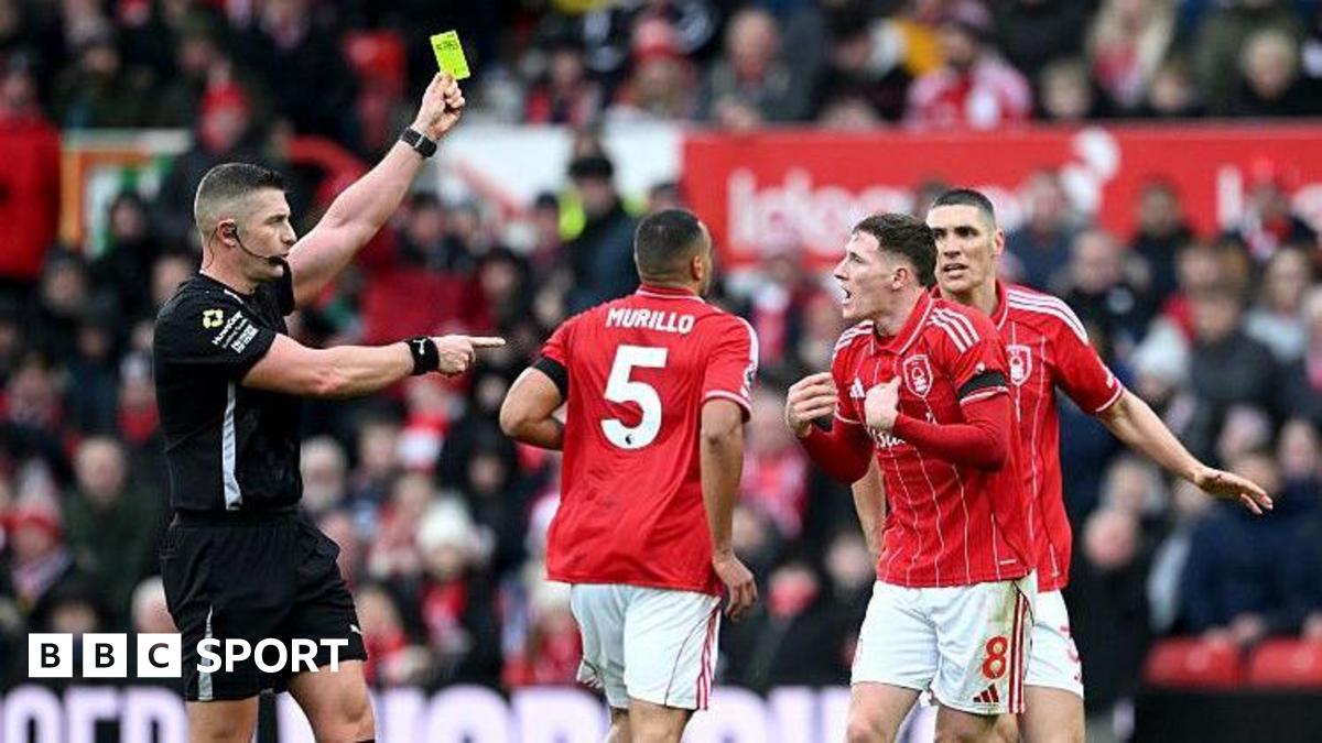 Referee Rob Jones books Elliot Anderson, with the official raising his yellow card above head height and pointing towards the animated Nottingham Forest player, in red and white, who has both hands out in front of his chest