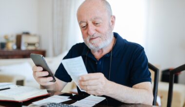 Senior man looking at bills and using his smartphone to budget and plan finances.