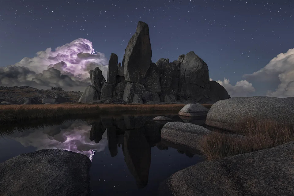 storm cloud with purple lightning moves over horizon. rock formations and reflective lake in foreground