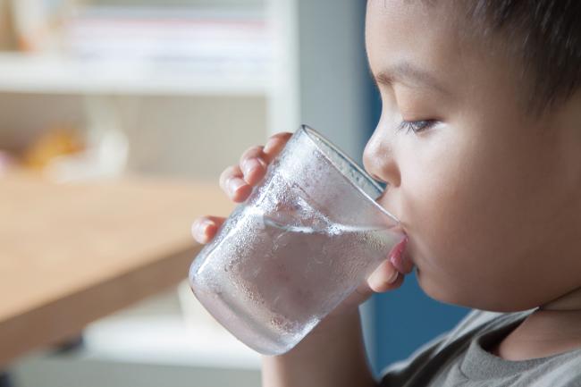 Young boy drinking a glass of water.