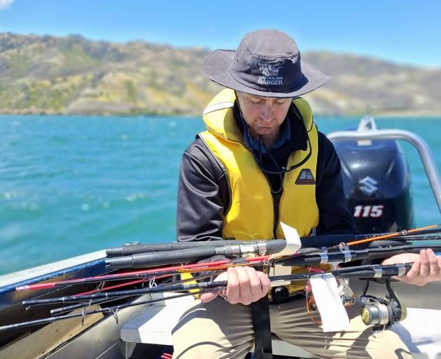 Otago Fish & Game officer Cole Briggs holds rods seized during compliance checks and angler...