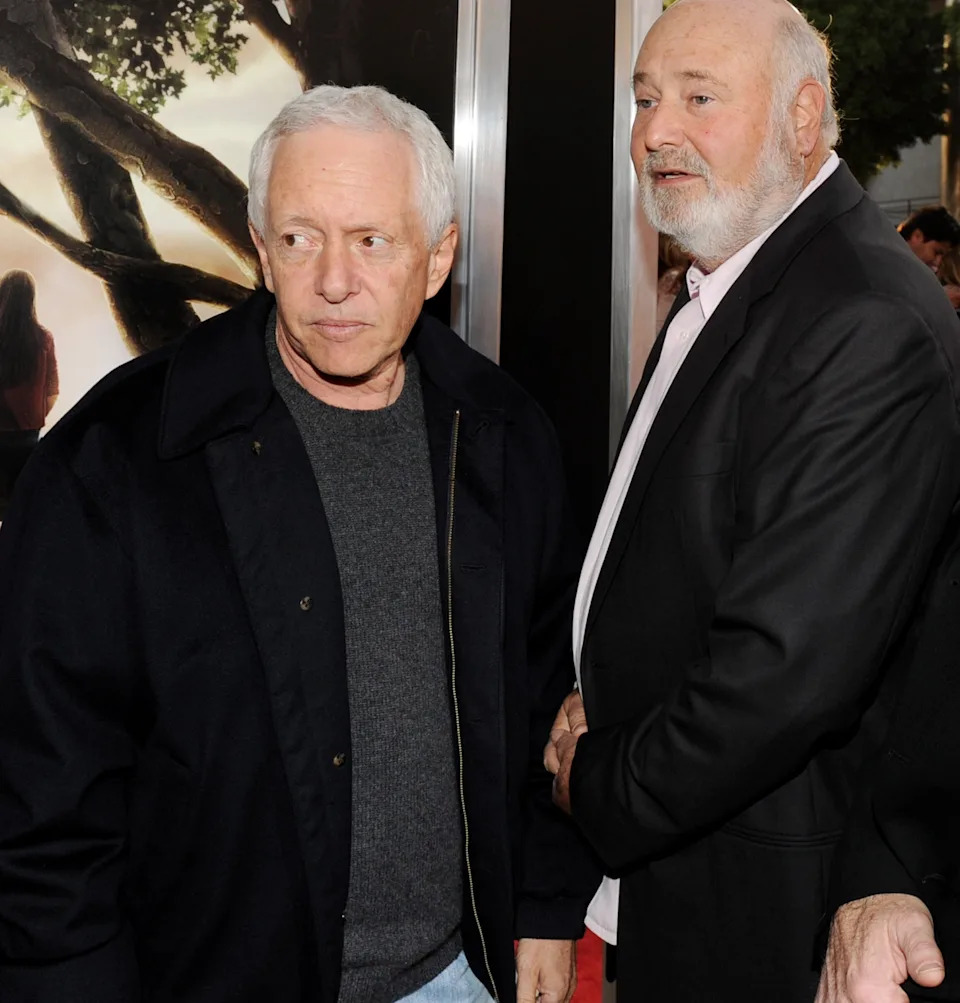 Three men in jackets stand at an event, looking to the side. A fourth person is partially visible behind them