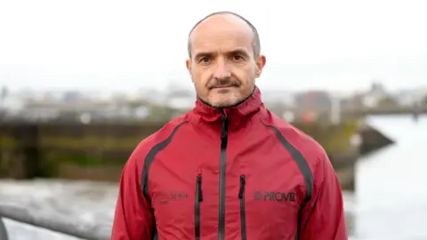 Gareth Clubb of WWF Cymru stands in front of Cardiff Bay barrage in a red waterproof coat