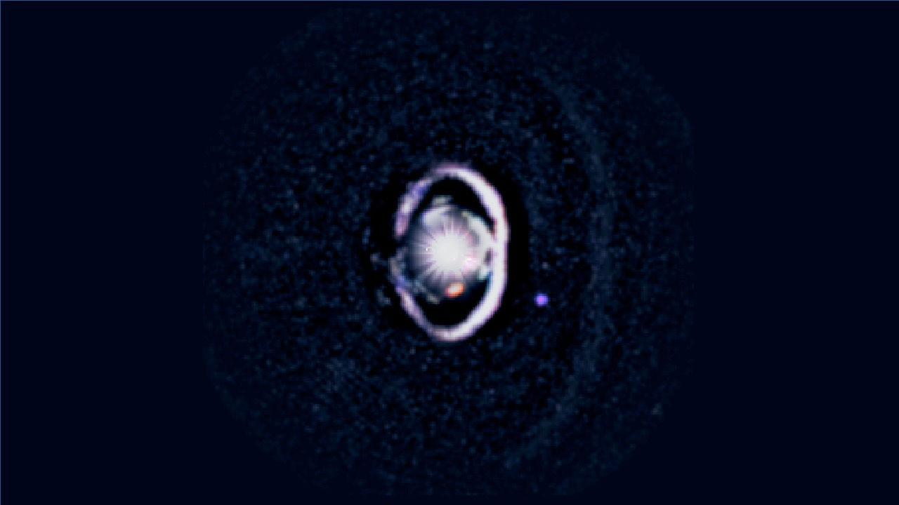 WISPIT 2b appears as a small purple dot beside a bright white dust ring encircling its star, with a fainter outer ring visible beyond it in new observations from the Magellan and Large Binocular Telescopes.