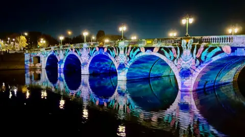 Lynne Falconer Worcester's river bridge illuminated with blue and pink lights creating five circles in the water