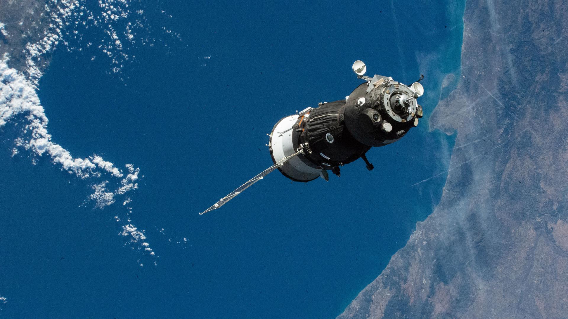 A gray spacecraft is seen floating above the ocean on Earth