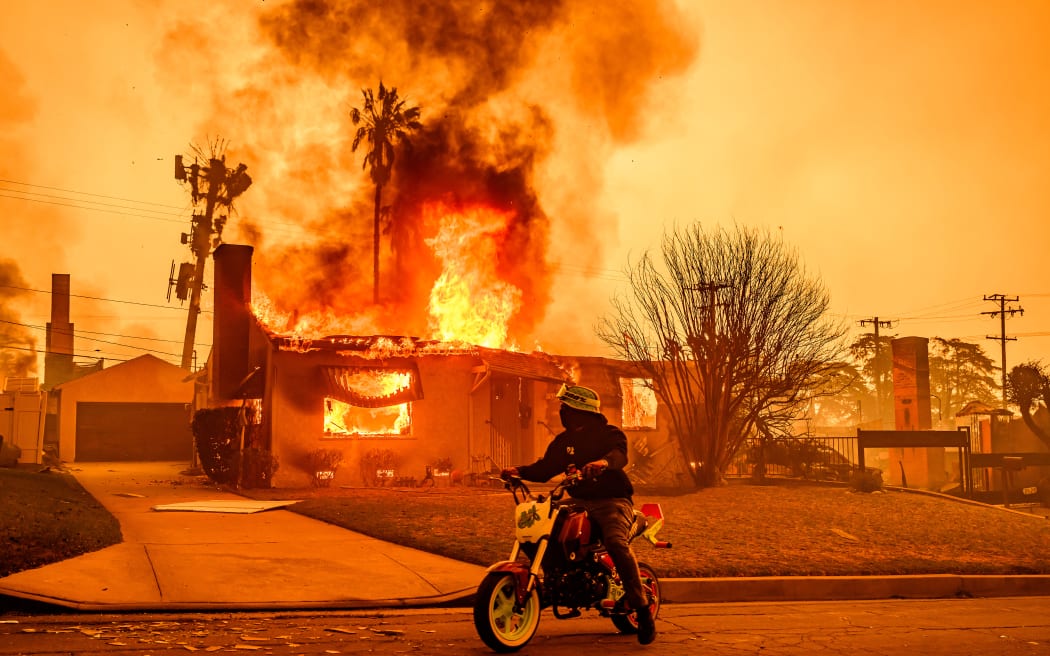 A motorcyclist stops to look at a burning home during the Eaton fire in the Altadena area of Los Angeles county, California on January 8, 2025. The United States' second-largest city had never faced a blaze of this scale, driven by an extreme autumn drought and fierce Santa Ana winds -- the strongest since 2011 -- that have turned dry hills into kindling, fuelling a relentless inferno that raged for more than a week.
