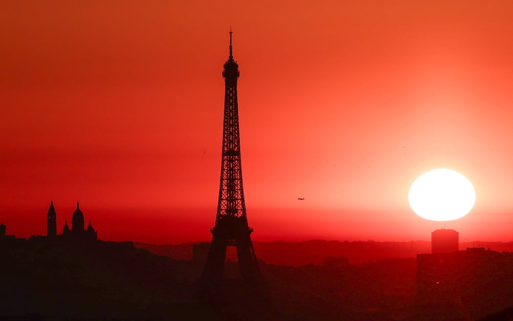 The sun rises by the Eiffel Tower and the Sacre Coeur Basilica on top of the Montmartre hill in Paris on July 1, 2025, as the city is on red alert for high temperatures, with the top of the Eiffel Tower shut, polluting traffic banned and speed restrictions in place as a searing heatwave gripped Europe.