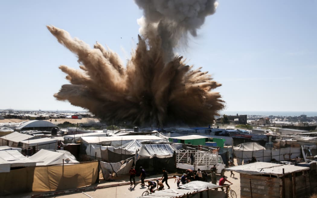 People run for cover as a plume of smoke rises above tents at a camp for displaced Palestinians in northern Khan Yunis in the southern Gaza Strip, during an Israeli strike on April 19, 2025.