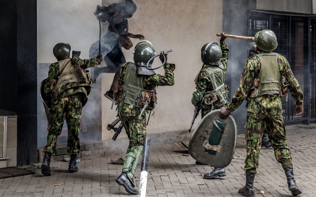 A protester jumps for safety as she emerges from a narrow alley while Kenya police officers strike her with whips and clubs during clashes in downtown Nairobi on June 25, 2025 during a planned day of protest marking the first anniversary of the storming of the parliament.