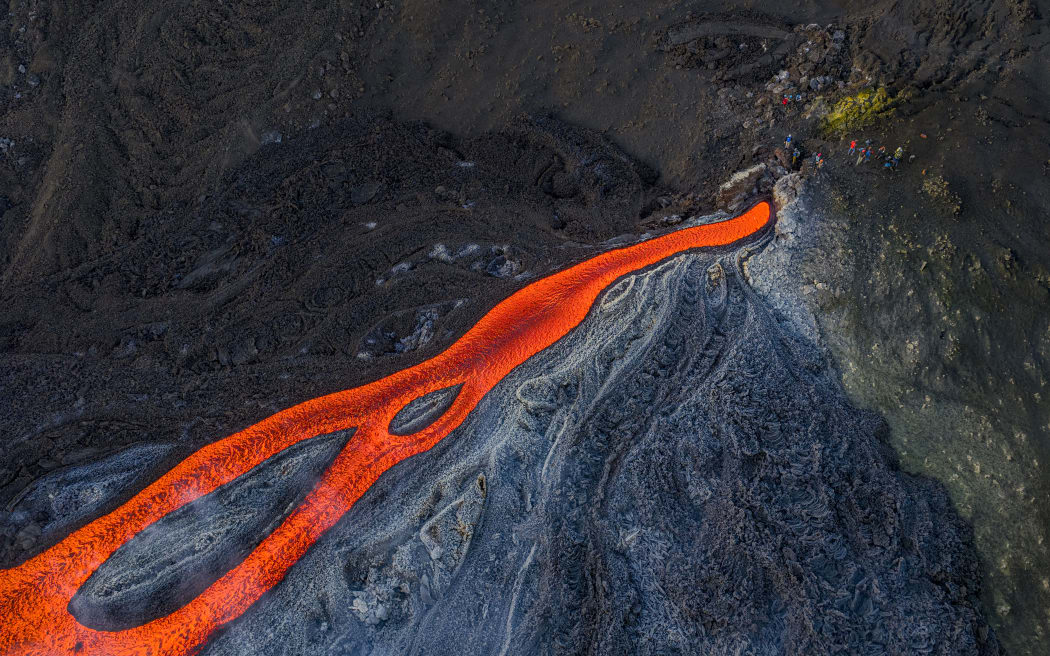 This aerial view shows people standing near a flow of lava from the Mount Etna volcano (Torre del Filosofo - Etna Sud) on August 28, 2025. The Etna volcanic eruption started on August 10 and remained active the last weeks.