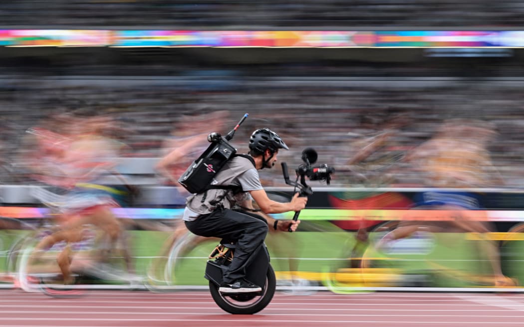 A cameraman on a unicycle films athletes in action as they compete in the men's 10000m final during the World Athletics Championships in Tokyo on September 14, 2025.