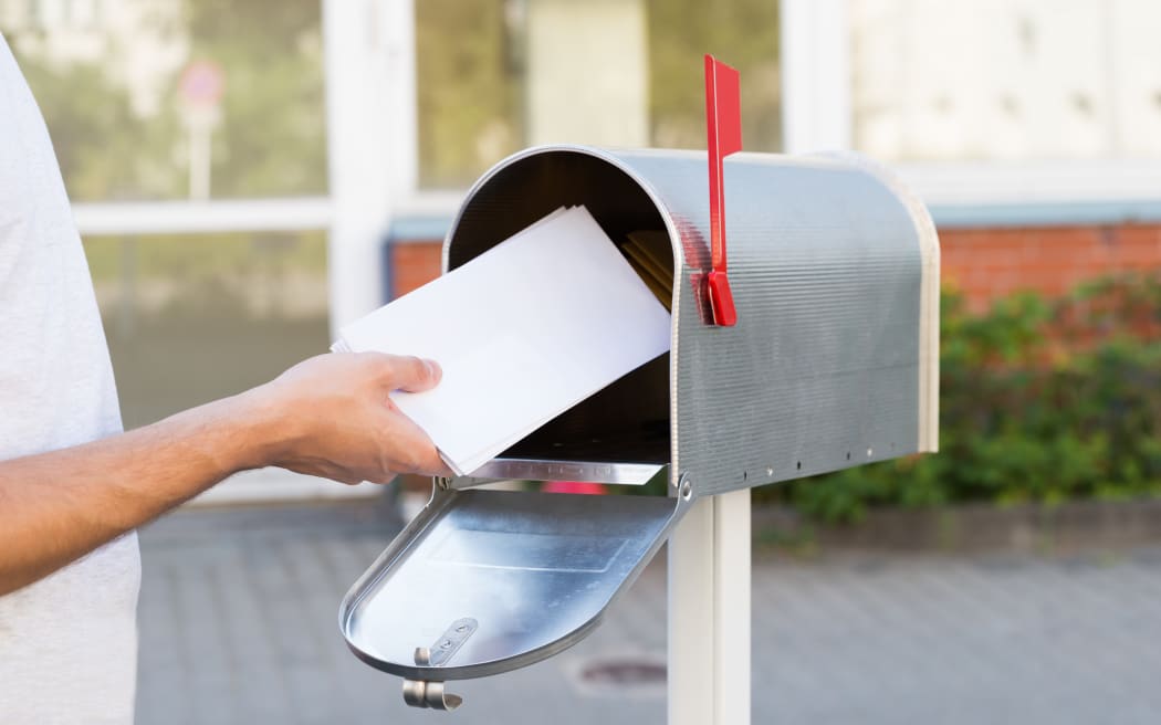 Close-up Of Person Putting Stack Of Letters In Mailbox