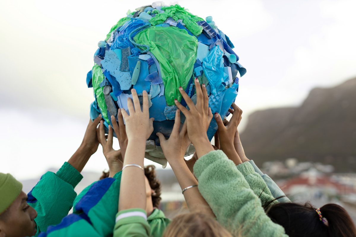 A group of people holding up an artwork of the Earth made of waste