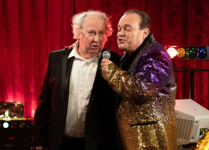540487,TITLE:Eastenders Nigel, in a black suit and white shirt, sings karaoke with Barry, who is in a sequinned gold and purple blazer in EastEnders