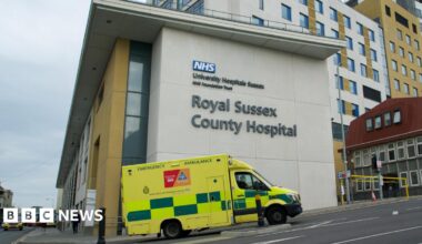 A hospital building in Brighton, East Sussex. It is modern-looking. An ambulance is driving by.