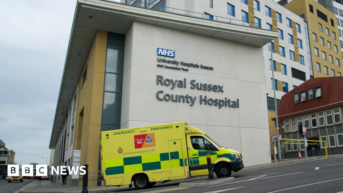 A hospital building in Brighton, East Sussex. It is modern-looking. An ambulance is driving by.
