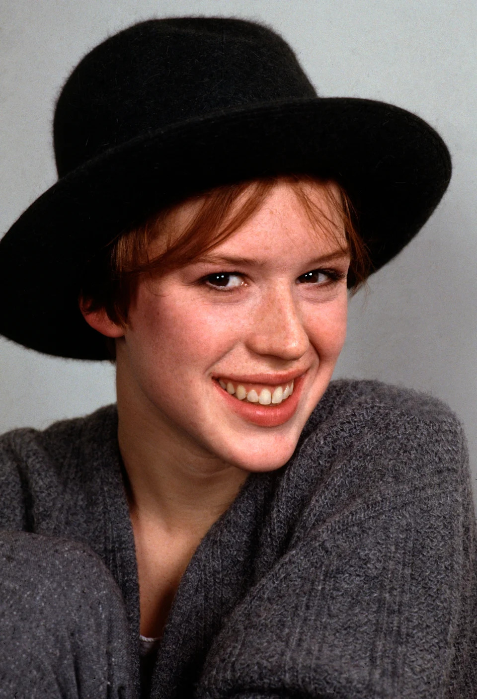 Person wearing a dark hat and textured sweater, smiling warmly at the camera