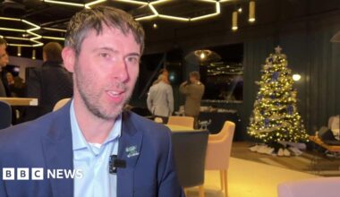 Neil Harris in a dark blue jacket at a launch event, with Christmas tree in the background
