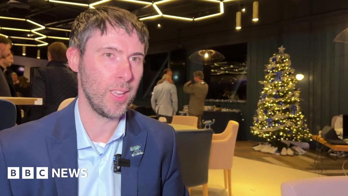Neil Harris in a dark blue jacket at a launch event, with Christmas tree in the background