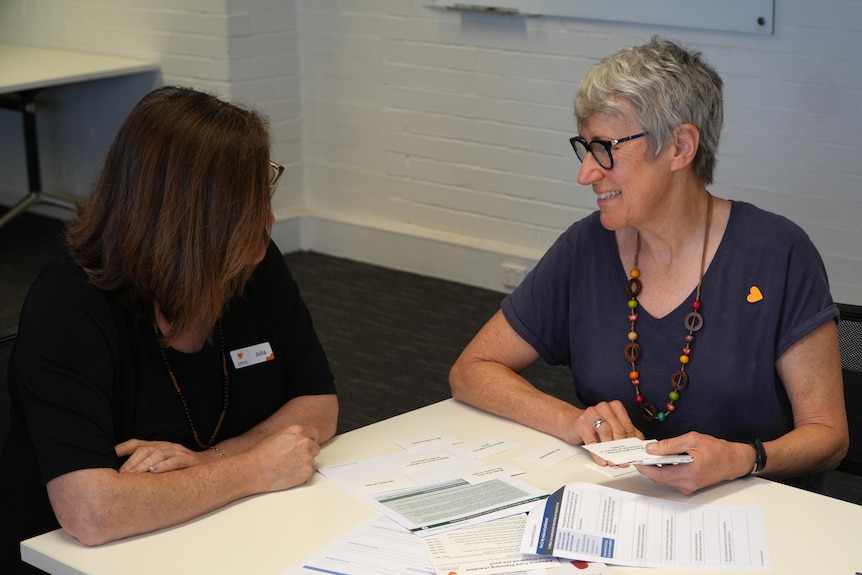 Two women sit at a table looking at papers. 