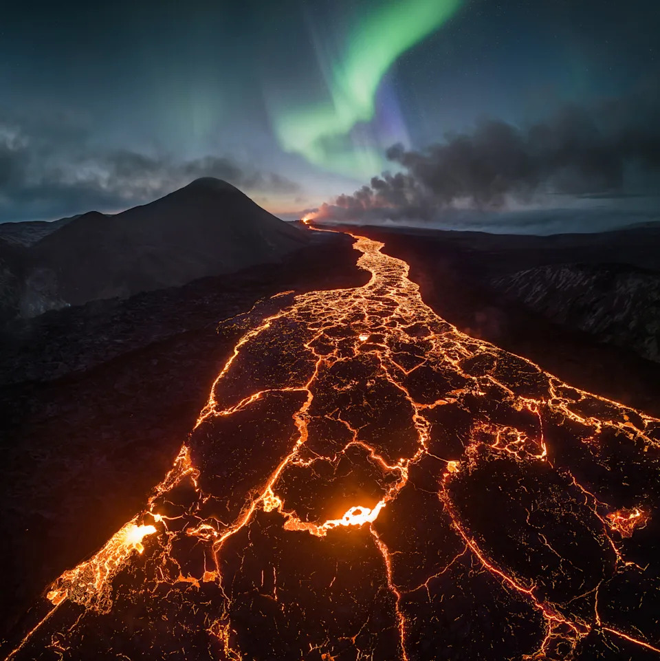 a river of lava moves under an aurora in Reykjanesbaer, Iceland
