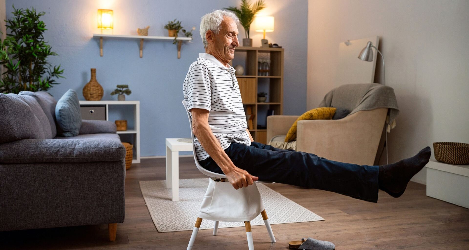 man in a striped tshirt sitting on a chair with legs outstretched with a living room setting behind him