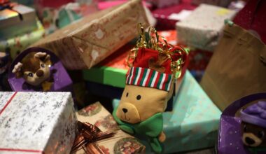 A variety of wrapped gifts and boxes, including a plush bear toy wearing a striped hat, are arranged in a festive setting.
