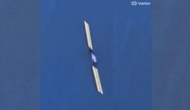 closeup photo taken from space of a boxy satellite with long, rectangular solar arrays extending on either side of its body