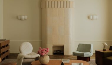 Image of a soft minimalist living room with white walls and curved shapes. There is a pastel stone, rounded fireplace, a curved wooden coffee table, and a mix of accent chairs around the room.