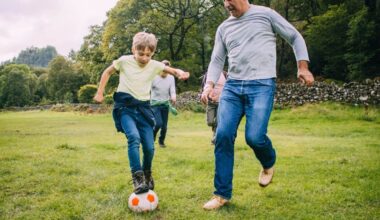 Three generation family are playing football together in a field. There are two boys, their father and their grandfather.