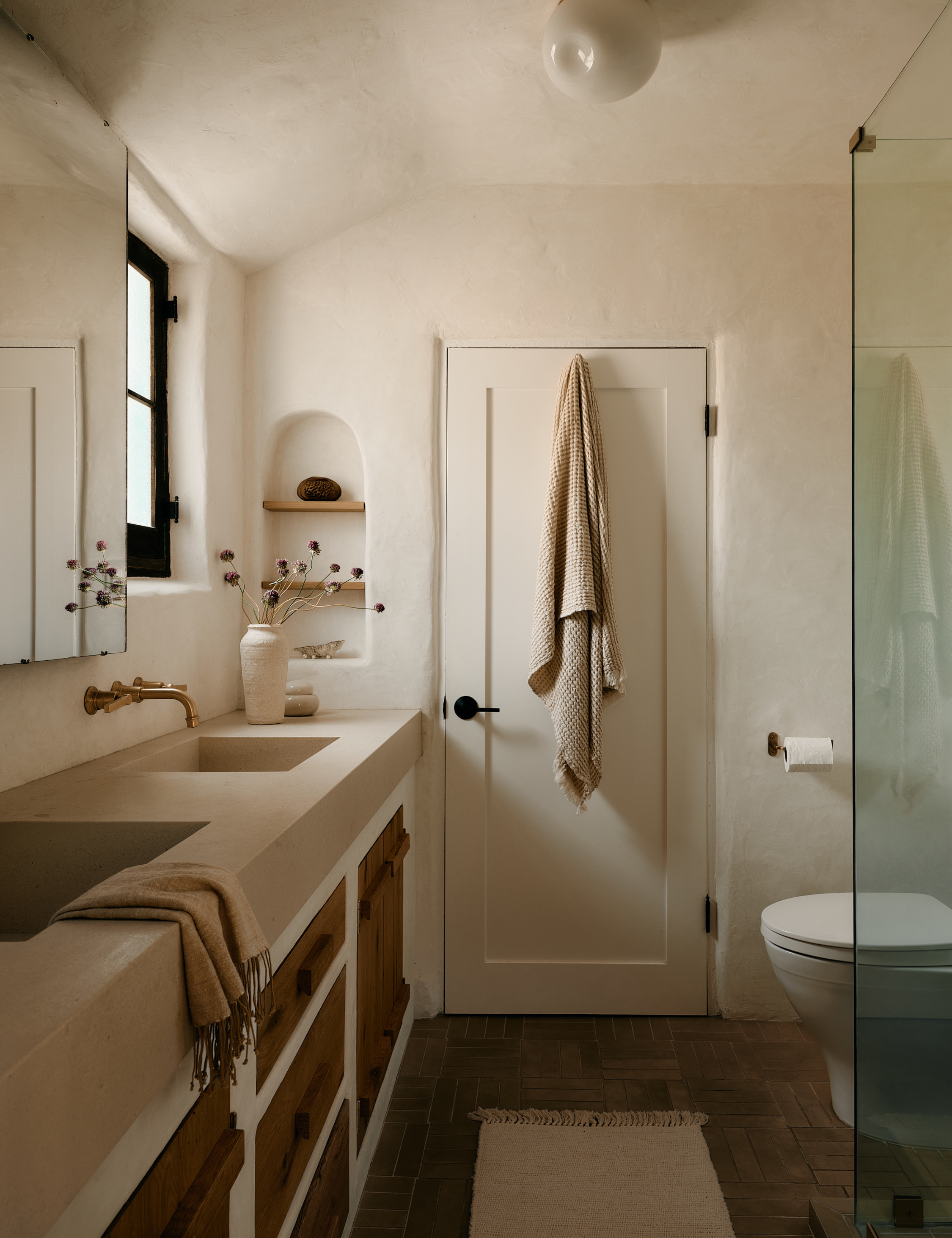 Sarah West Interiors-designed bathroom featuring parquet tile floors, plaster walls, and aged brass hardware accents