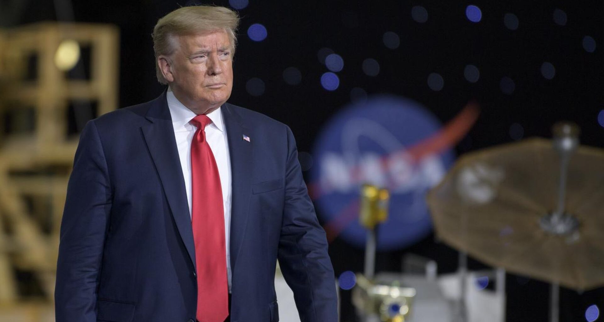 President Donald Trump in a red tie surrounded by NASA hardware