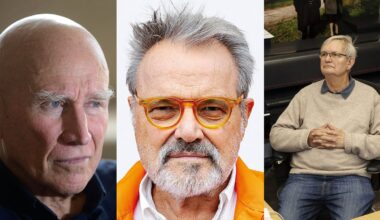 Three older men; the first is bald and gazing to the side, the second has gray hair, a beard, orange glasses, and an orange jacket, and the third has gray hair, glasses, and is sitting with hands clasped.