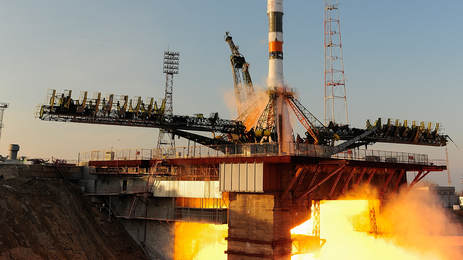 Photo of a rocket firing its engines with its fiery exhaust passing through a hole in the launch pad