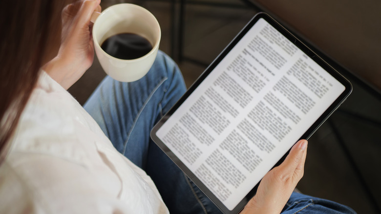 Woman holding coffee cup and tablet with text on.