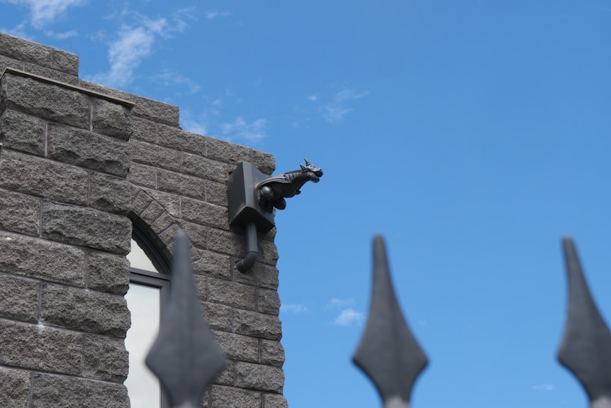 Dark grey 3D printed gargoyles attached to the side of an imitation bluestone castle/house.