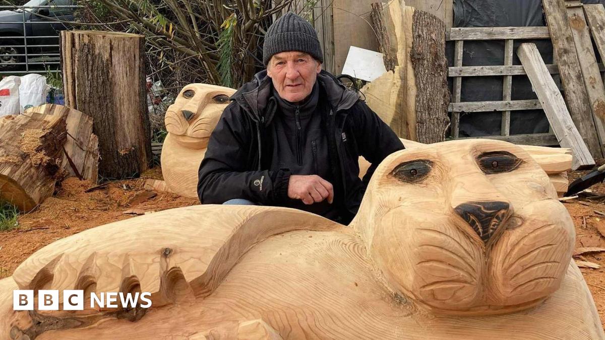 Ste Iredale is crouching behind one of the new seal sculptures. It has been hand-carved and there is a second one behind Mr him. He is wearing a hat and a black coat.