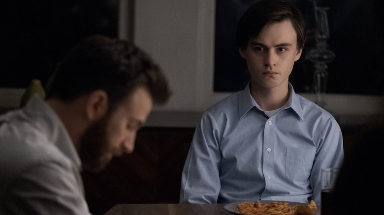 Andy (Chris Evans) looking down with Jacob (Jaeden Martell) sat at the head of a table on Defending Jacob