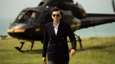 Happy Prince/Disney+ David Tennant's Tony Baddingham striding away from a helicopter
